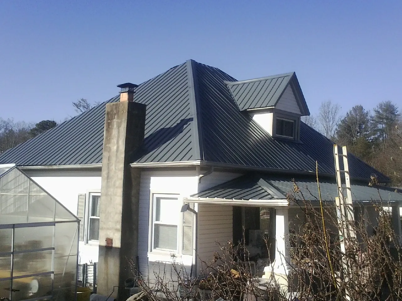 Dark blue standing seam metal roof on a white farmhouse with dormer — Slate & Tile Roof Repair by Roofing Brothers in Whitehall