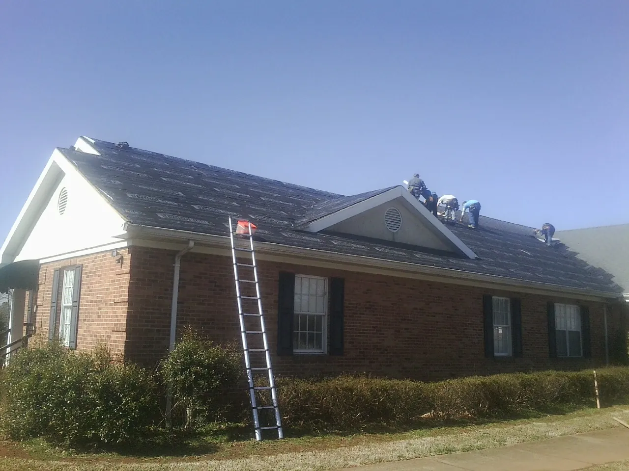 Crew tearing shingles off a brick ranch roof with a ladder set — Metal Roof Repair work by our crew in Whitehall
