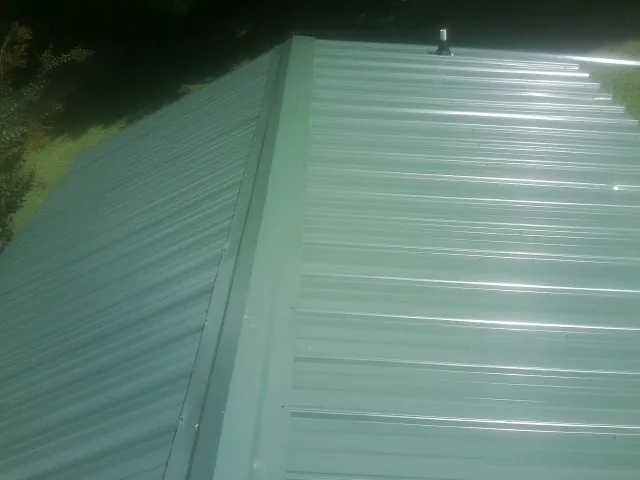 New green metal panels meeting at the ridge of a roof — Flat Roof Repair work by our crew in Whitehall