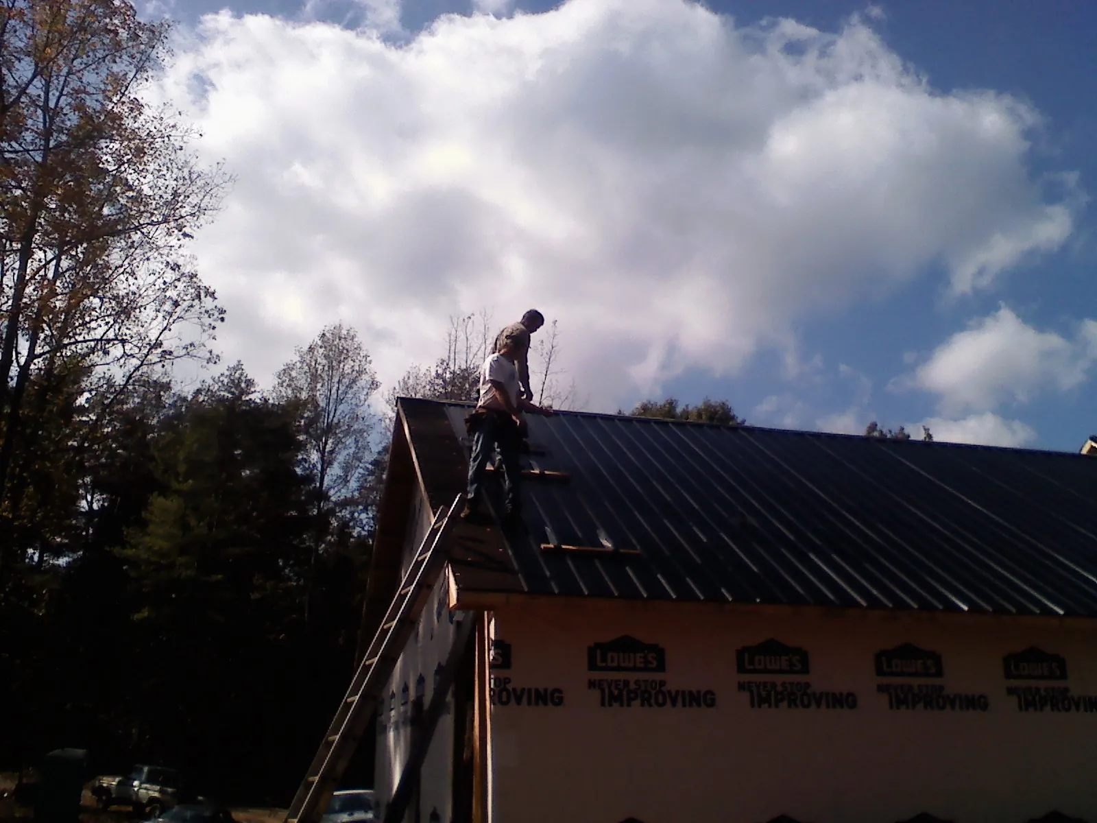 Roofer fastening dark metal panels high against a cloudy sky, from a Roof Inspection job in Whitehall